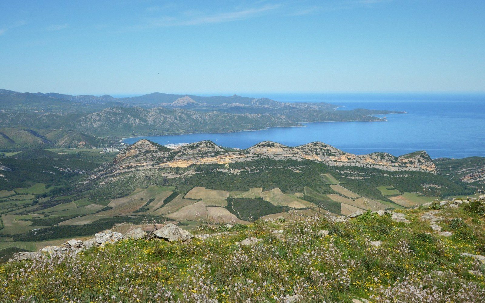 Rocky ridgeline and farmland stretch toward a coastal bay under a clear sky