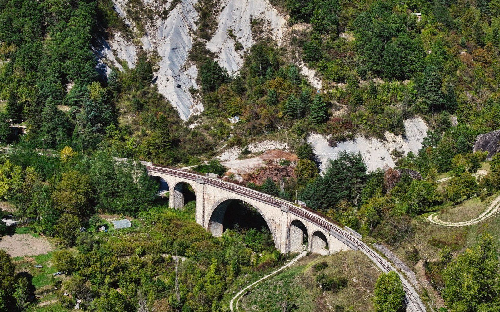 Aerial view of a stone railway viaduct with multiple arches crossing a forested mountainside