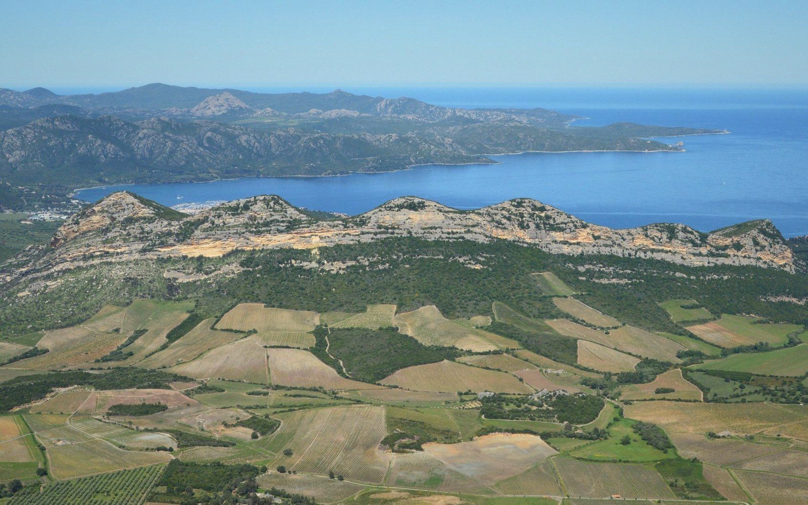 Aerial view of patchwork farmland and vineyards below a rocky ridge meeting the coastline