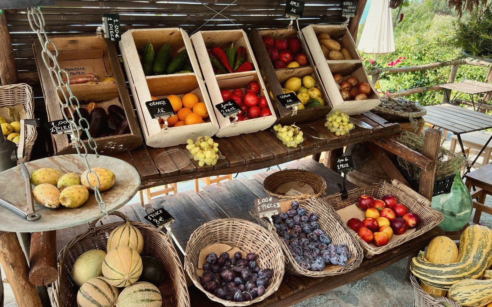 A market stall table loaded with local produce — tomatoes, melons, bunched herbs — seen from above