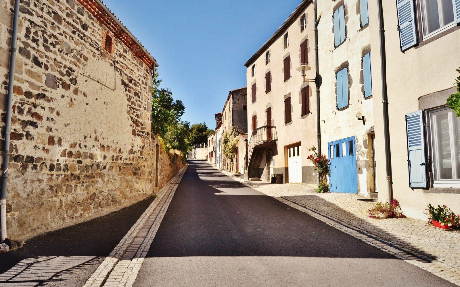 A narrow stone lane in a perched village, shutters closed, midday light cutting a hard shadow across the paving